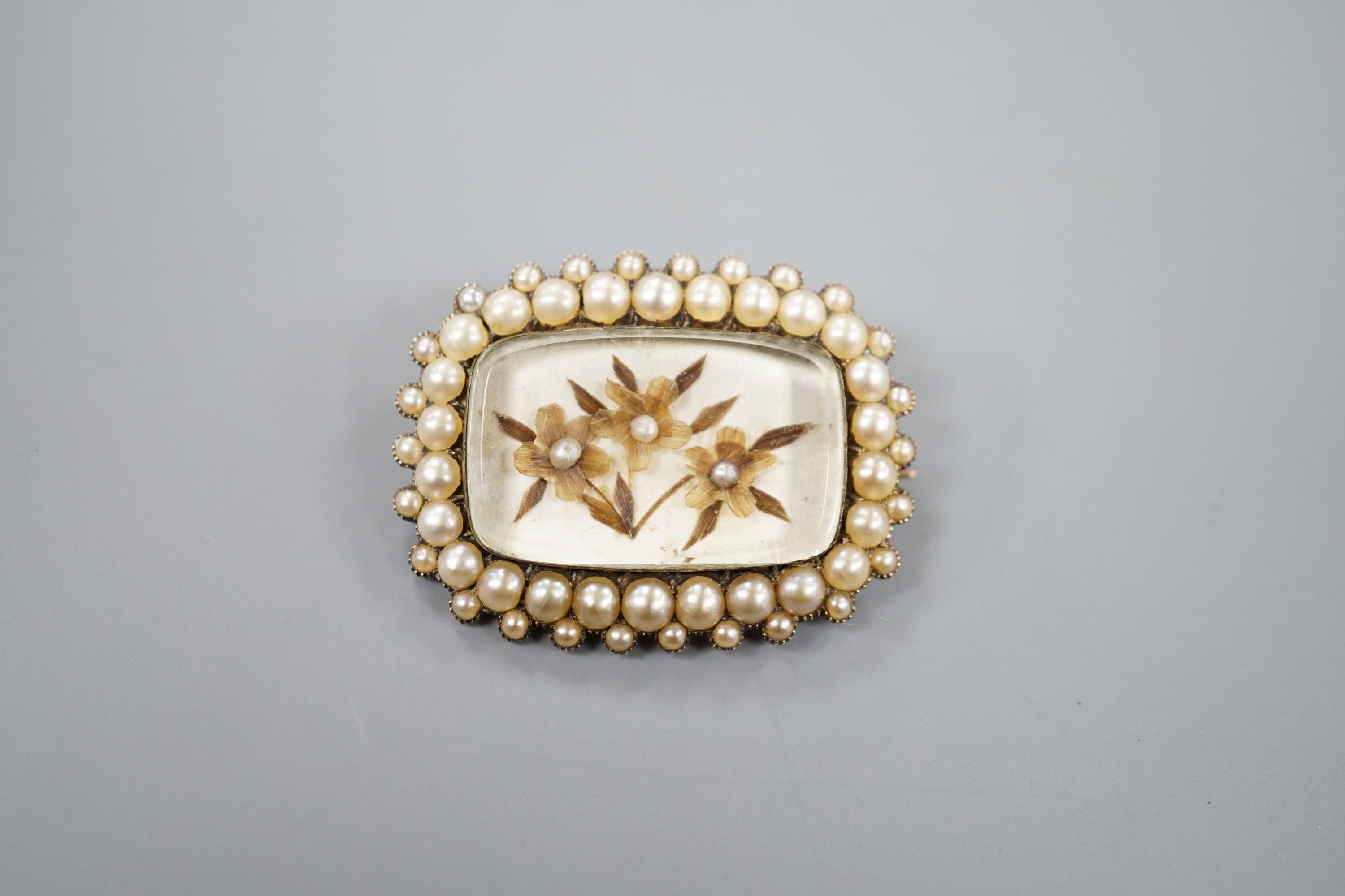 A 19th century yellow metal and seed pearl brooch, with glazed floral motif, 31mm, gross weight 6.1 grams.